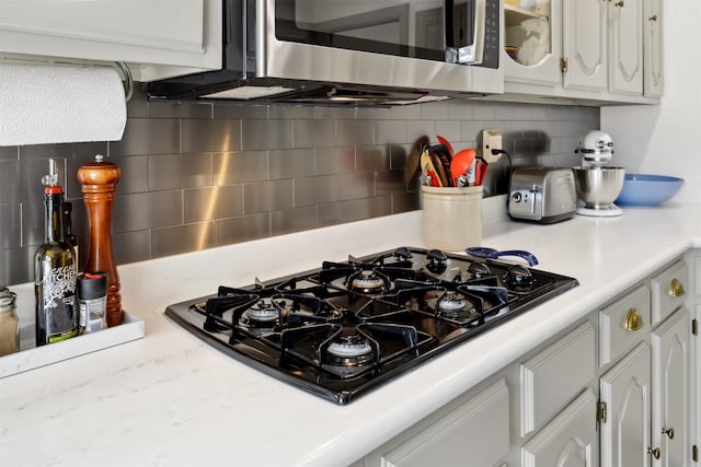 kitchen with black gas cooktop, stainless steel microwave, backsplash, light countertops, and white cabinetry