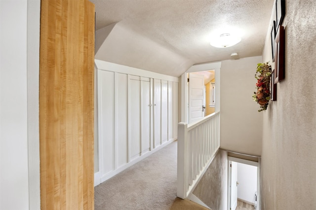 corridor featuring lofted ceiling, a textured ceiling, an upstairs landing, and carpet flooring