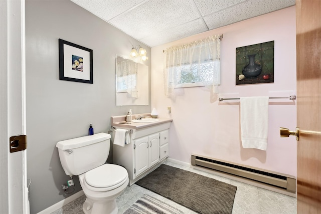 bathroom with a baseboard radiator, a drop ceiling, toilet, vanity, and baseboards