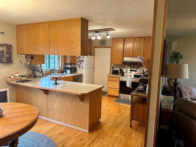 146 New Meadows Dr, Missoula, MT 59808 - kitchen with appliances with stainless steel finishes, under cabinet range hood, light wood-type flooring, a peninsula, and light countertops