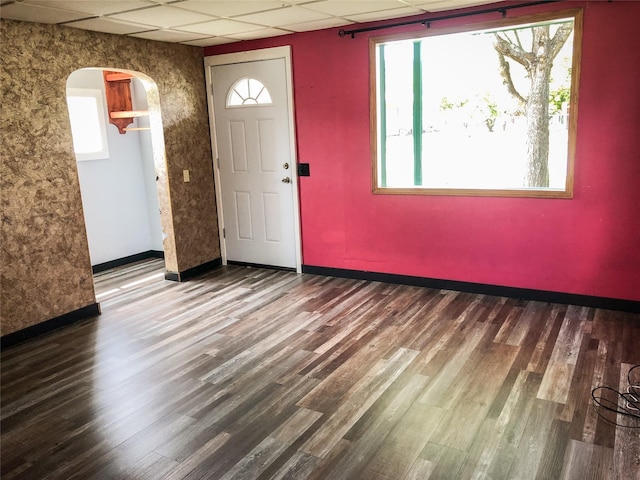 foyer entrance with a drop ceiling, arched walkways, baseboards, and wood finished floors