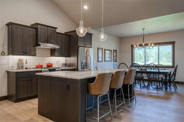 29 Elk Run Trl, Kalispell, MT 59901 - kitchen featuring light wood-style floors, under cabinet range hood, dark brown cabinets, tasteful backsplash, and light stone countertops
