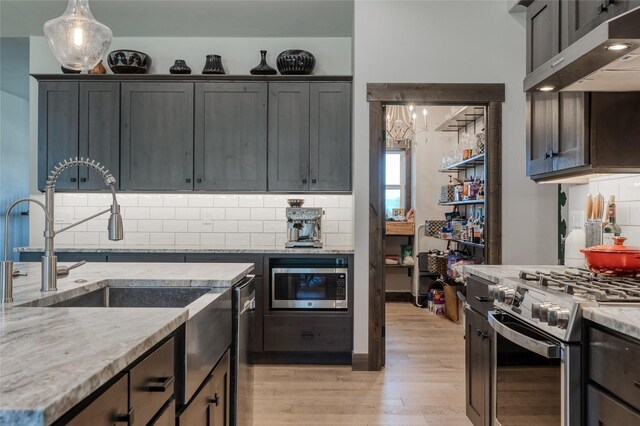 29 Elk Run Trl, Kalispell, MT 59901 - kitchen with appliances with stainless steel finishes, range hood, light wood finished floors, light stone countertops, and decorative backsplash