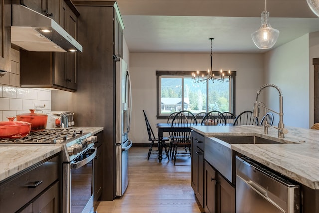 29 Elk Run Trl, Kalispell, MT 59901 - kitchen featuring wall chimney exhaust hood, appliances with stainless steel finishes, light wood finished floors, dark brown cabinets, and a chandelier