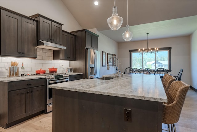29 Elk Run Trl, Kalispell, MT 59901 - kitchen featuring appliances with stainless steel finishes, under cabinet range hood, vaulted ceiling, a kitchen bar, and decorative backsplash