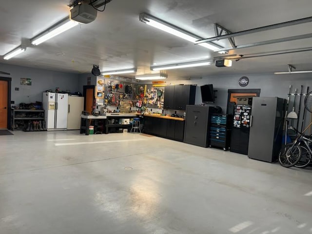 36496 Ridgeway Ct, Polson, MT 59860 - garage with a workshop area, white refrigerator with ice dispenser, a garage door opener, and freestanding refrigerator