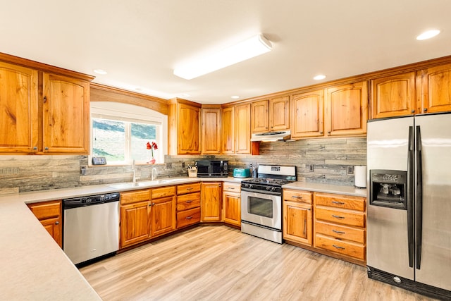 kitchen featuring appliances with stainless steel finishes, light countertops, under cabinet range hood, backsplash, and light wood finished floors