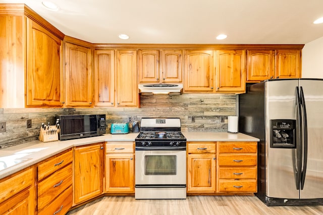 kitchen featuring appliances with stainless steel finishes, under cabinet range hood, light wood-type flooring, light countertops, and tasteful backsplash