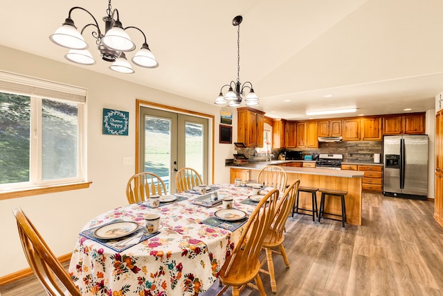 dining area with a chandelier, light wood-style floors, french doors, and vaulted ceiling