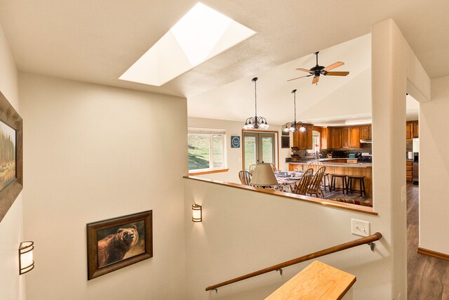 stairs with wood finished floors, vaulted ceiling, a skylight, a ceiling fan, and baseboards