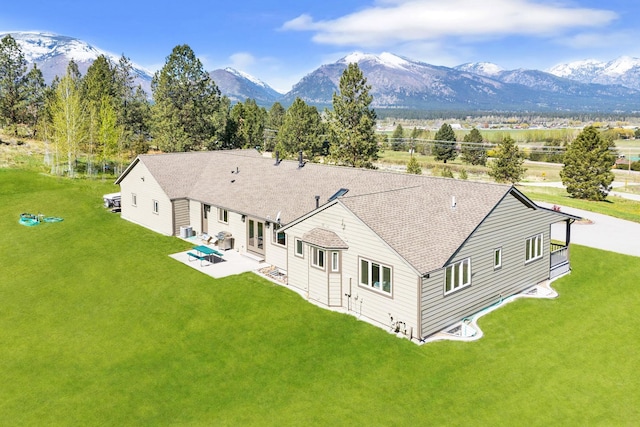 rear view of house with a patio, a mountain view, a yard, and roof with shingles