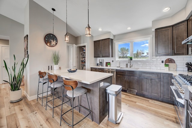 kitchen with a sink, stainless steel appliances, a breakfast bar, dark brown cabinetry, and tasteful backsplash