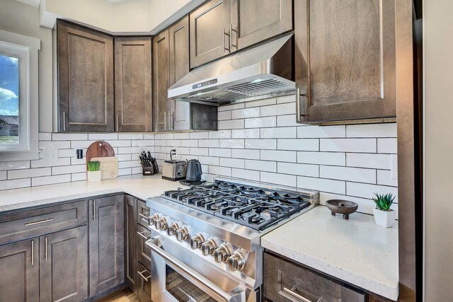 kitchen with under cabinet range hood, stainless steel range, tasteful backsplash, and dark brown cabinetry