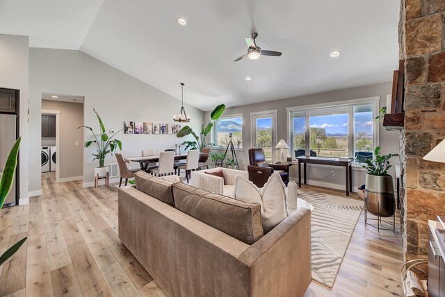 living area featuring washing machine and dryer, a ceiling fan, lofted ceiling, light wood finished floors, and a chandelier