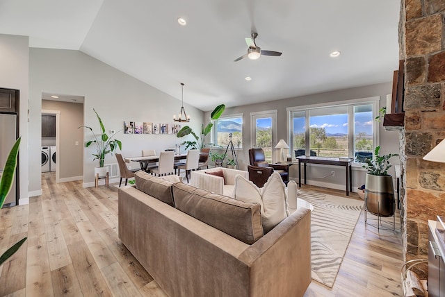 living area featuring washing machine and dryer, a ceiling fan, lofted ceiling, light wood finished floors, and a chandelier