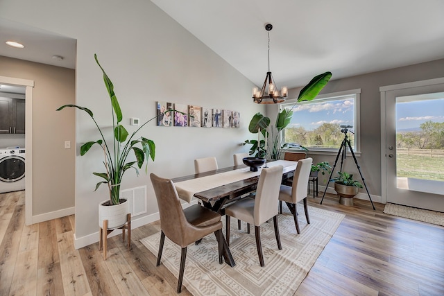 dining area featuring washer / dryer, baseboards, light wood-style floors, a chandelier, and lofted ceiling