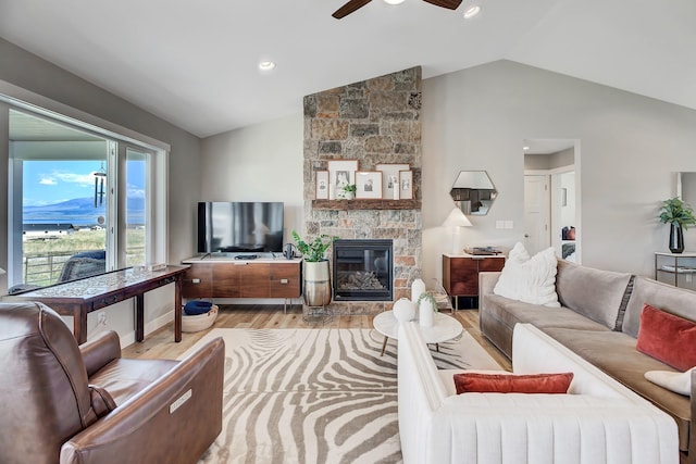 living area with wood finished floors, vaulted ceiling, a ceiling fan, and a stone fireplace