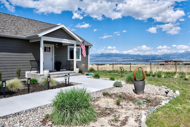 view of exterior entry with a mountain view, covered porch, fence, and a shingled roof