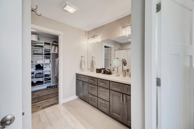 full bath featuring wood finished floors, double vanity, a spacious closet, and baseboards