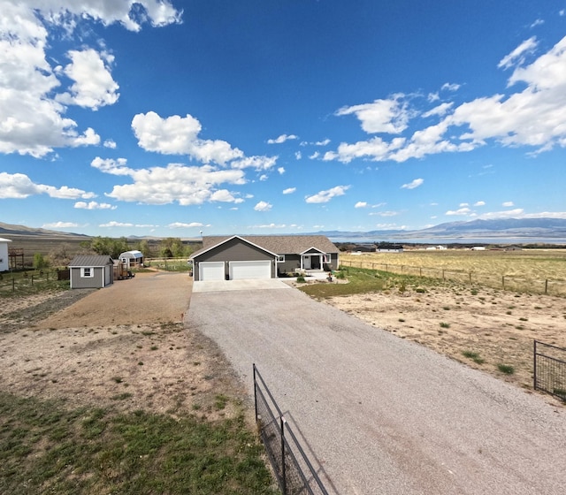 view of front of home with fence, gravel driveway, a view of rural / pastoral area, a garage, and a shed