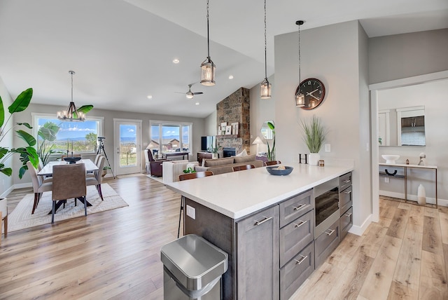kitchen with a fireplace, gray cabinets, light wood-style floors, light countertops, and high vaulted ceiling