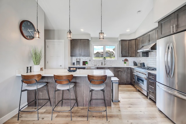 kitchen with appliances with stainless steel finishes, under cabinet range hood, dark brown cabinetry, a breakfast bar area, and recessed lighting