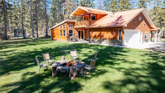 1492 Mcmannamy Draw, Kalispell, MT 59901 - rear view of house featuring a trampoline, an outdoor fire pit, a garage, a yard, and a balcony
