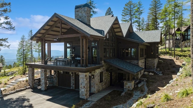145 Elk Highlands Dr, Whitefish, MT 59937 - back of house featuring stone siding, roof with shingles, a chimney, driveway, and a carport