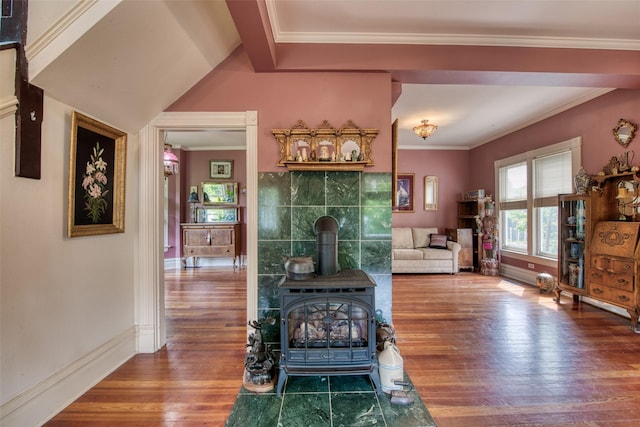 living area with wood finished floors, baseboards, a wood stove, and ornamental molding