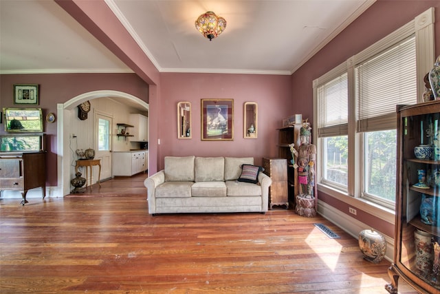 living area featuring wood-type flooring, ornamental molding, arched walkways, and baseboards