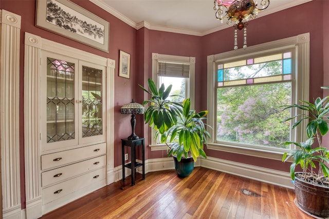 living area with healthy amount of natural light, wood-type flooring, baseboards, a chandelier, and crown molding