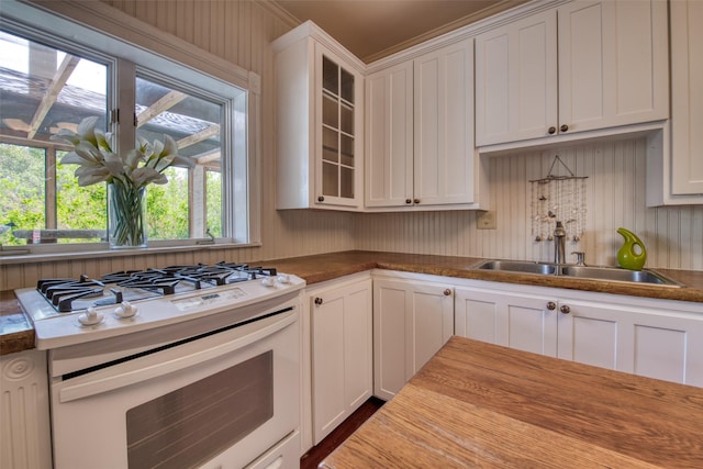 kitchen with white gas range oven, a sink, white cabinets, and glass insert cabinets