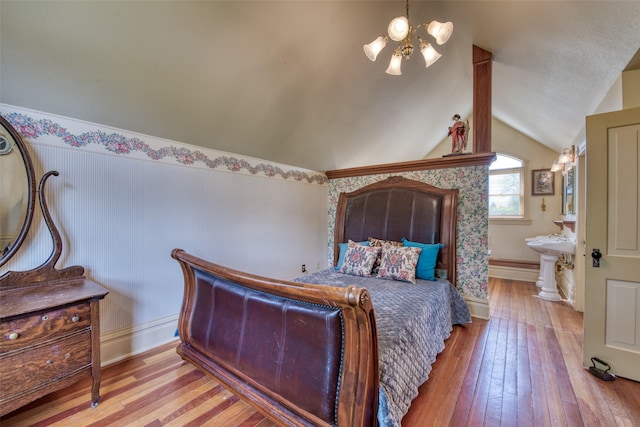 bedroom featuring wood-type flooring, a chandelier, vaulted ceiling, baseboards, and ensuite bath