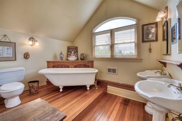 full bath featuring wood-type flooring, lofted ceiling, a freestanding tub, baseboards, and toilet