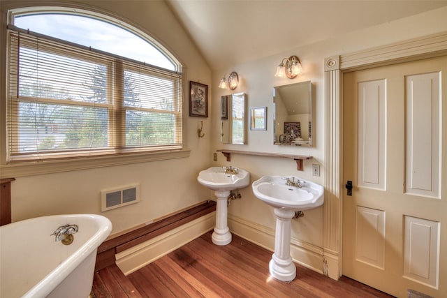 full bath with lofted ceiling, a soaking tub, wood finished floors, and baseboards
