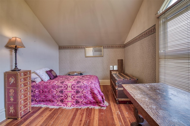 bedroom featuring lofted ceiling, wallpapered walls, and wood finished floors