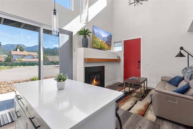 living room featuring a towering ceiling, wood finished floors, a glass covered fireplace, and baseboards
