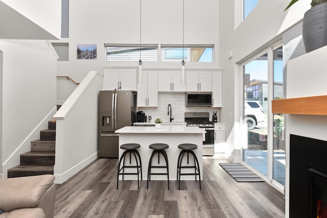 kitchen with appliances with stainless steel finishes, a breakfast bar, a towering ceiling, wood finished floors, and a kitchen island