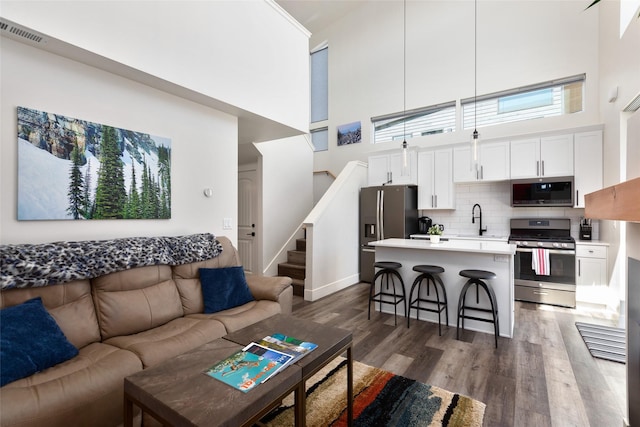 living area featuring a high ceiling, dark wood-style flooring, stairway, and baseboards