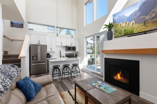 living area featuring a towering ceiling, healthy amount of natural light, dark wood finished floors, stairway, and a glass covered fireplace