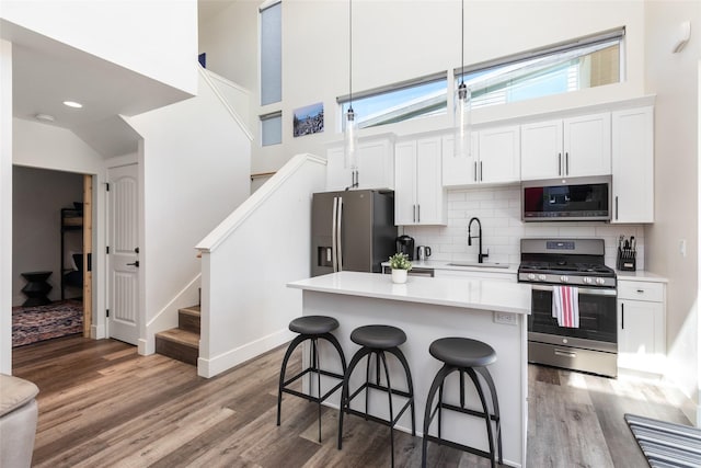 kitchen with appliances with stainless steel finishes, a kitchen bar, a sink, wood finished floors, and backsplash
