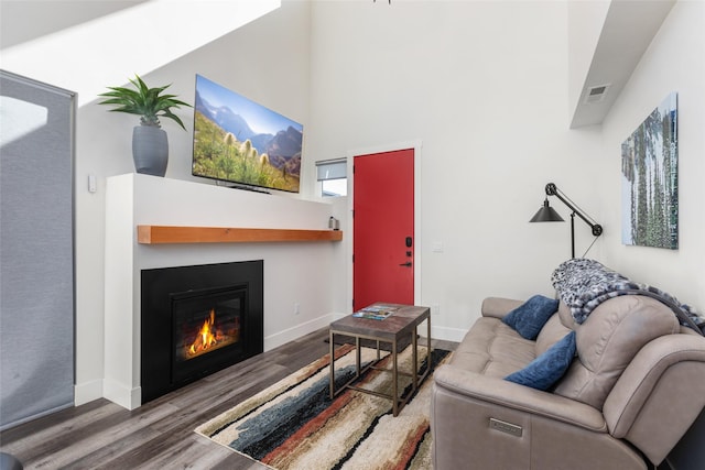 living area with wood finished floors, a glass covered fireplace, baseboards, and a high ceiling