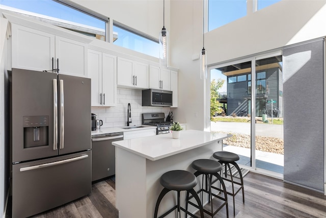 kitchen featuring stainless steel appliances, a sink, dark wood-type flooring, light countertops, and a kitchen breakfast bar
