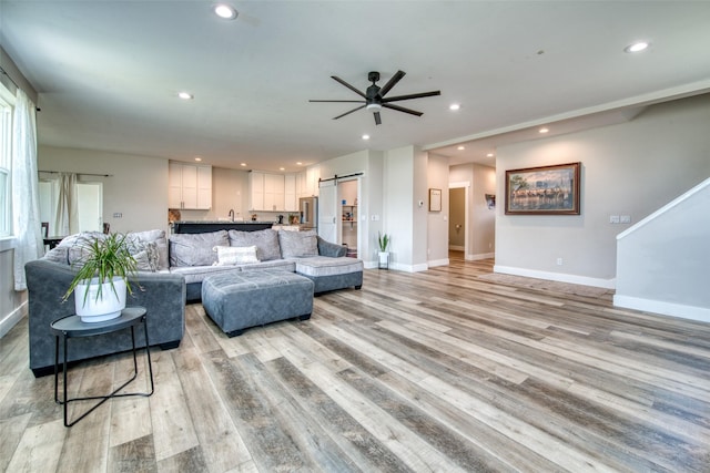 living area with recessed lighting, a ceiling fan, baseboards, light wood-style flooring, and a barn door