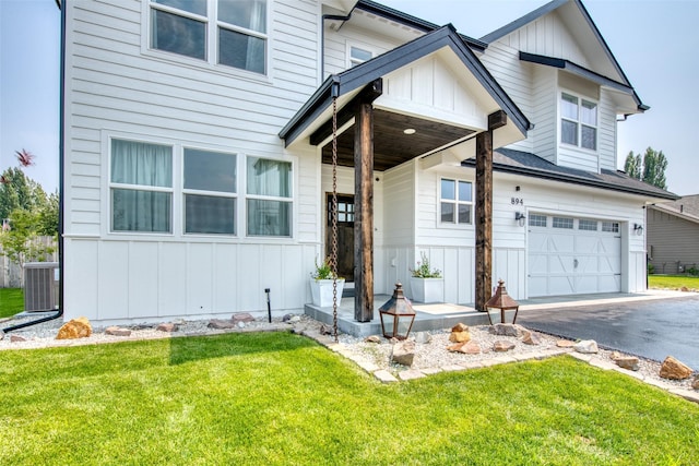 view of front of property with board and batten siding, a front lawn, an attached garage, driveway, and central AC