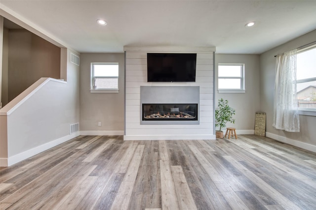 unfurnished living room with wood finished floors, a fireplace, baseboards, healthy amount of natural light, and recessed lighting