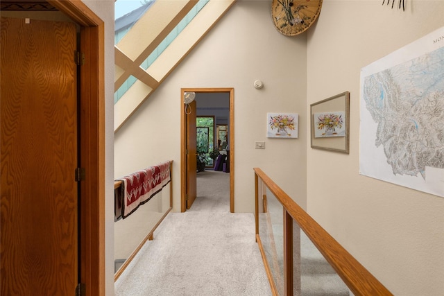 corridor featuring light colored carpet, a skylight, a high ceiling, and an upstairs landing