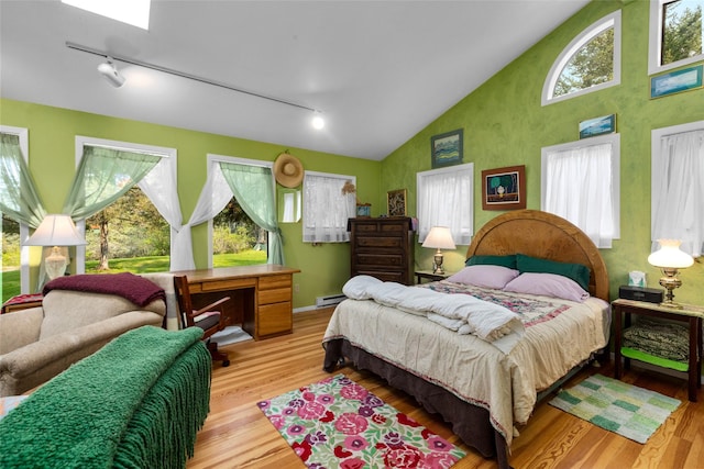 bedroom featuring rail lighting, light wood-type flooring, baseboard heating, and high vaulted ceiling