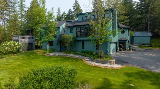 view of front of home featuring an attached garage, driveway, a front yard, and an outbuilding