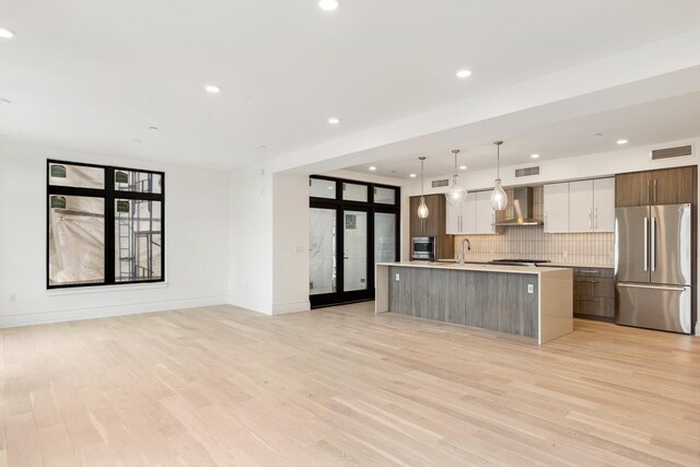 315 N Tracy Ave Unit 404, Bozeman, MT 59715 - kitchen featuring appliances with stainless steel finishes, wall chimney range hood, modern cabinets, open floor plan, and light countertops